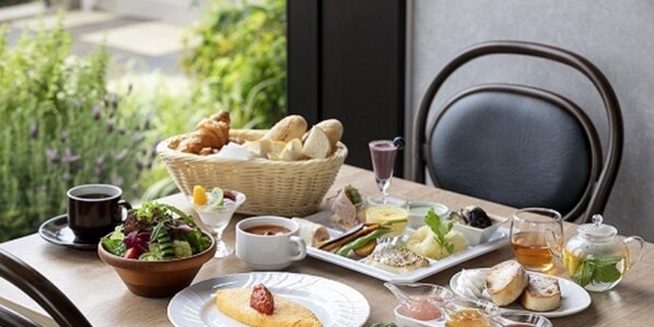 Een gedekte tafel met verschillende gerechten, waaronder brood, salade en gebak, met uitzicht op groen buiten.