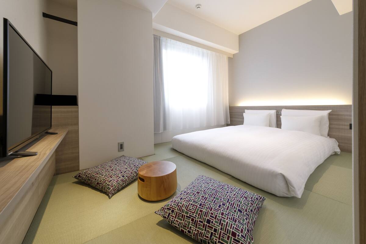 A modern hotel room with a large bed, a flat-screen TV, and a large window with curtains.