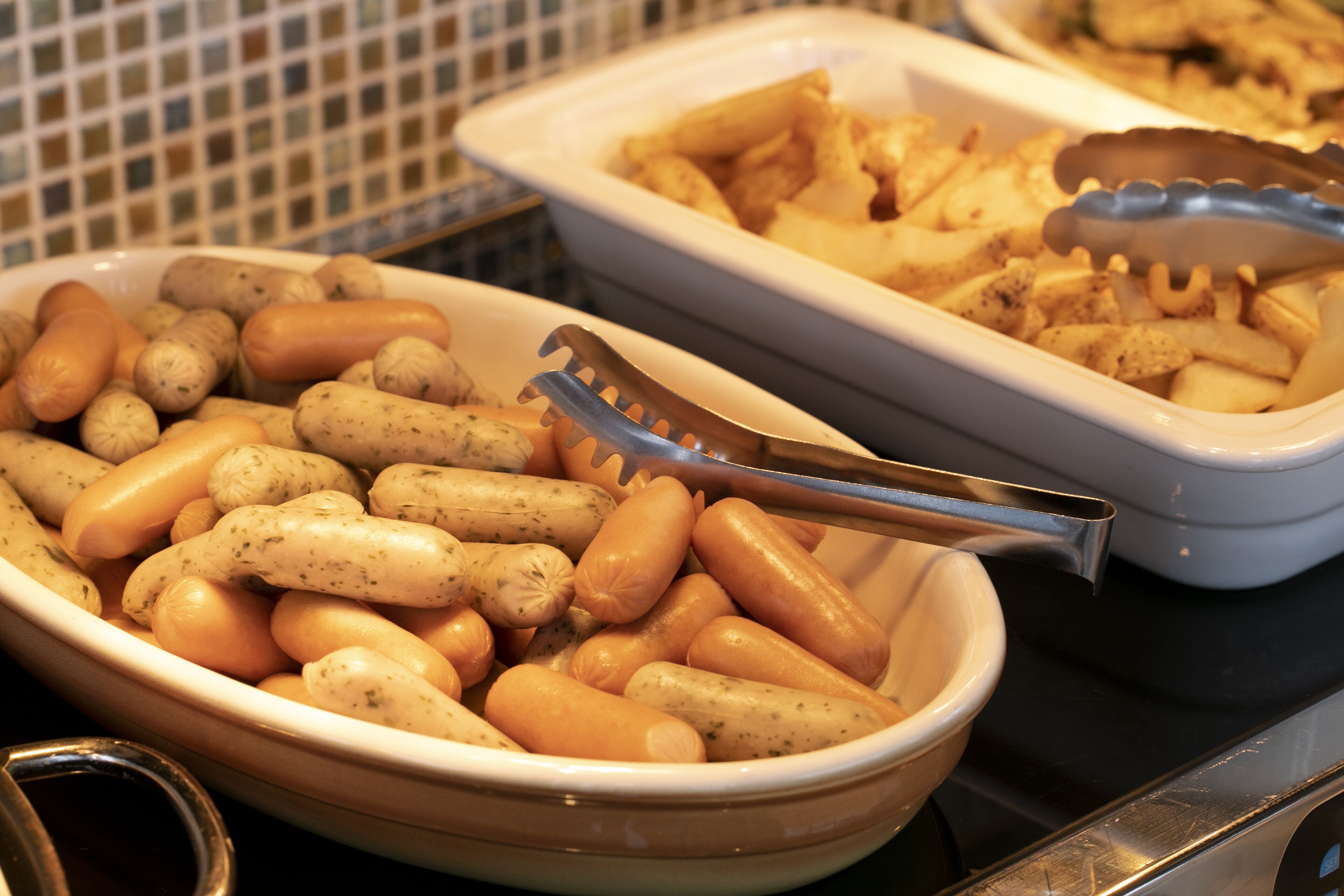 Una mesa de bufé con diversos platos, incluyendo salchichas y pasta.