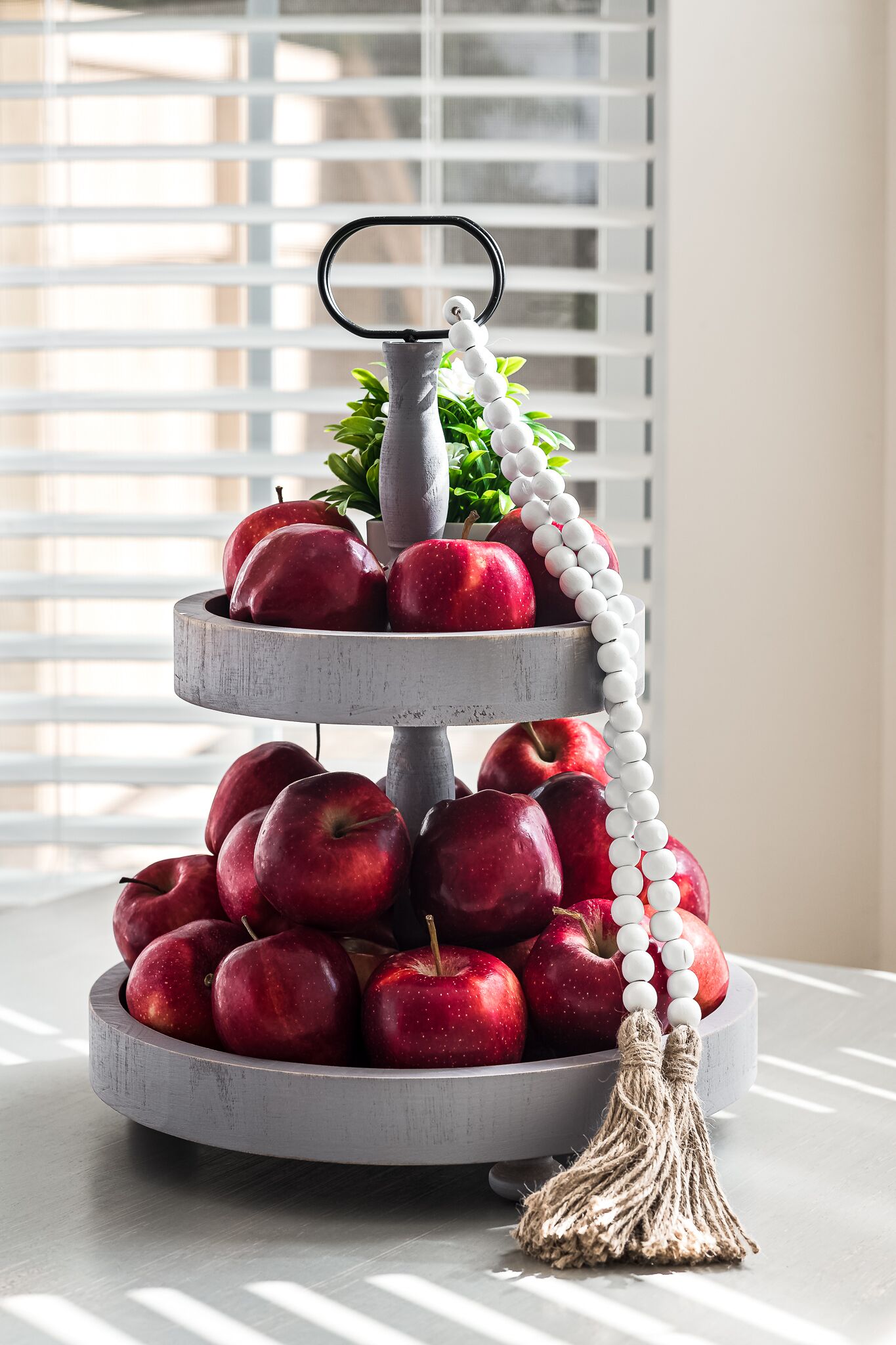 A three-tiered fruit stand with apples and a decorative tassel.