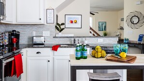 A modern kitchen with white cabinets, a brick backsplash, and a countertop with a coffee maker, toaster, and bottles of Pellegrino water. - The Ol' Cottage @ Davidson  (Davidson)