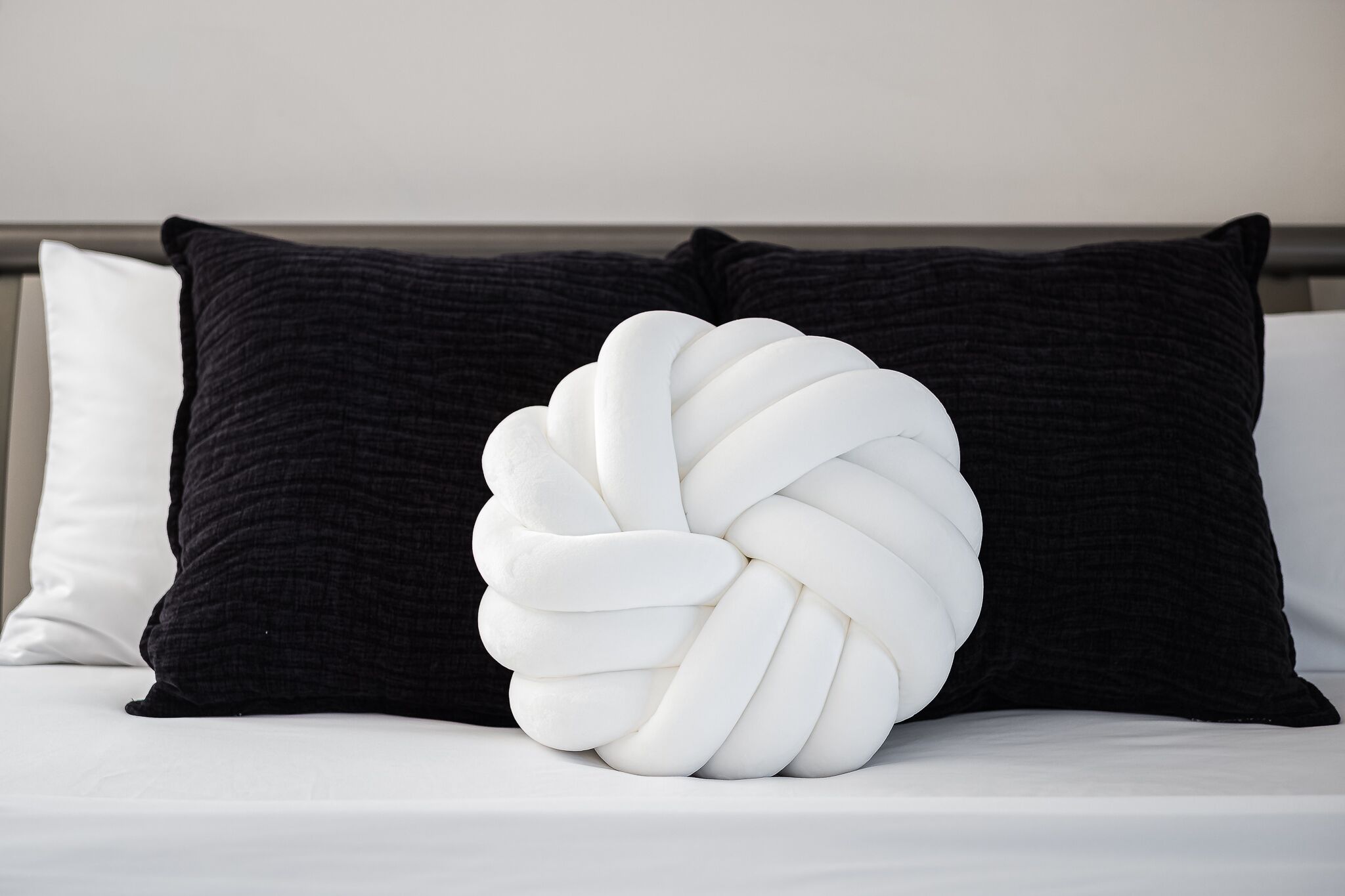 A bed with a unique white, twisted pillow design and two dark pillows.