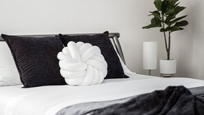 A neatly made bed with white and dark pillows, a black throw blanket, and a bedside plant. - The Ol' Cottage @ Davidson  (Davidson)