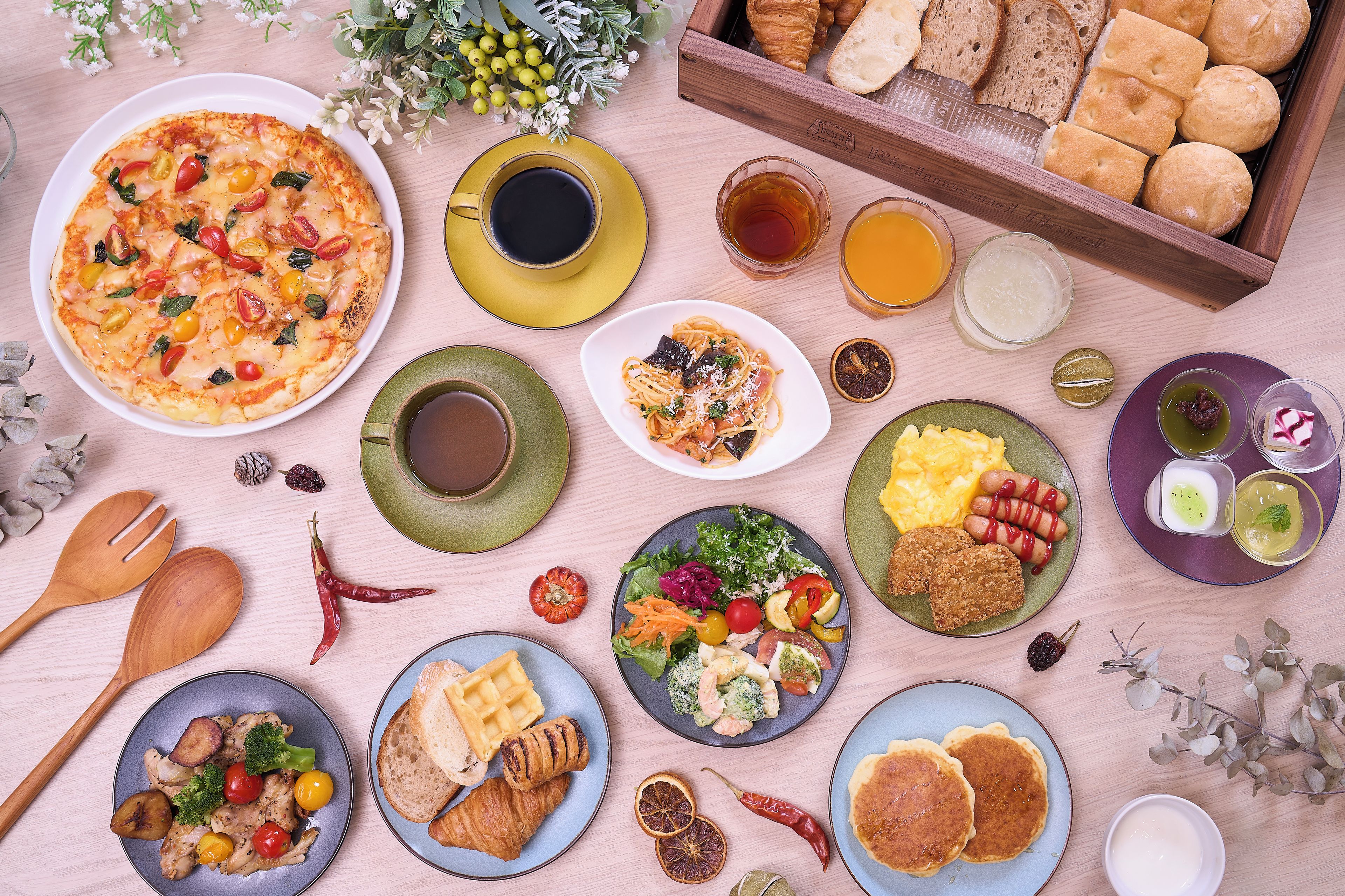 A variety of dishes and food items arranged on a table, including a pizza, bread, and various salads.