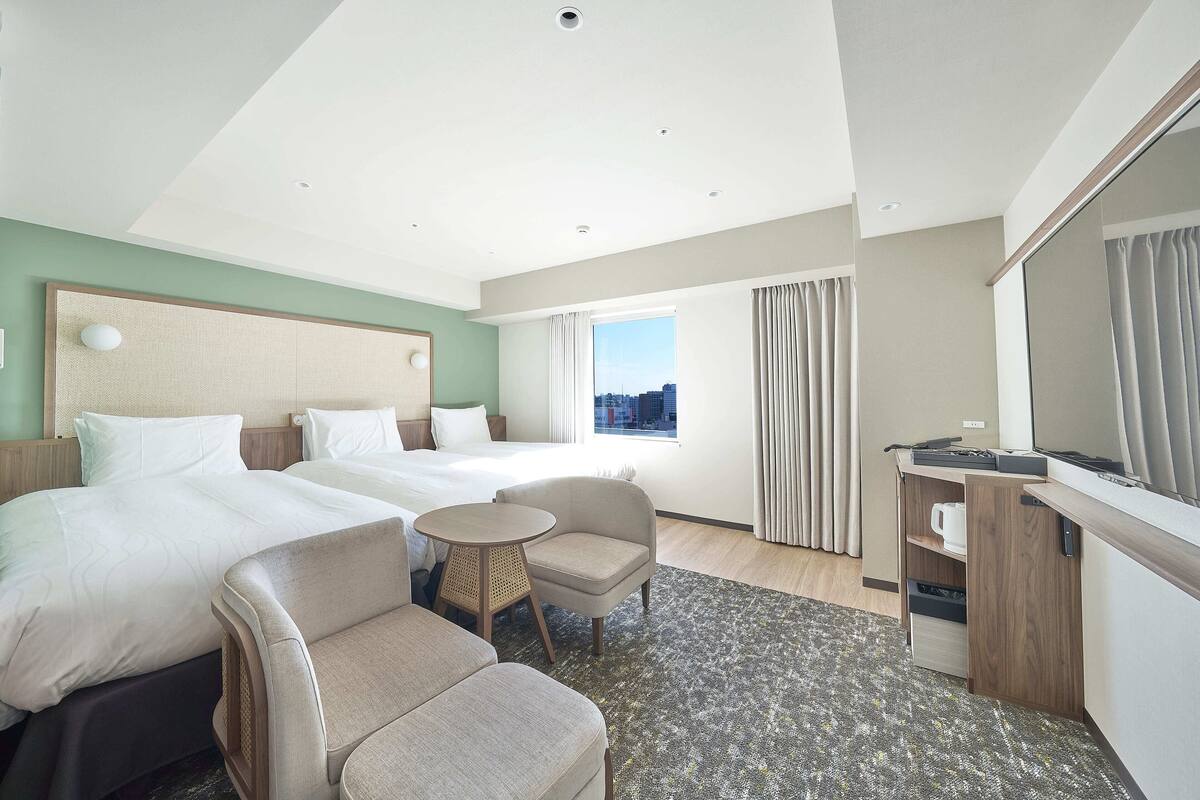 Een hotelkamer met twee bedden, een bureau, een stoel en uitzicht op de stad.