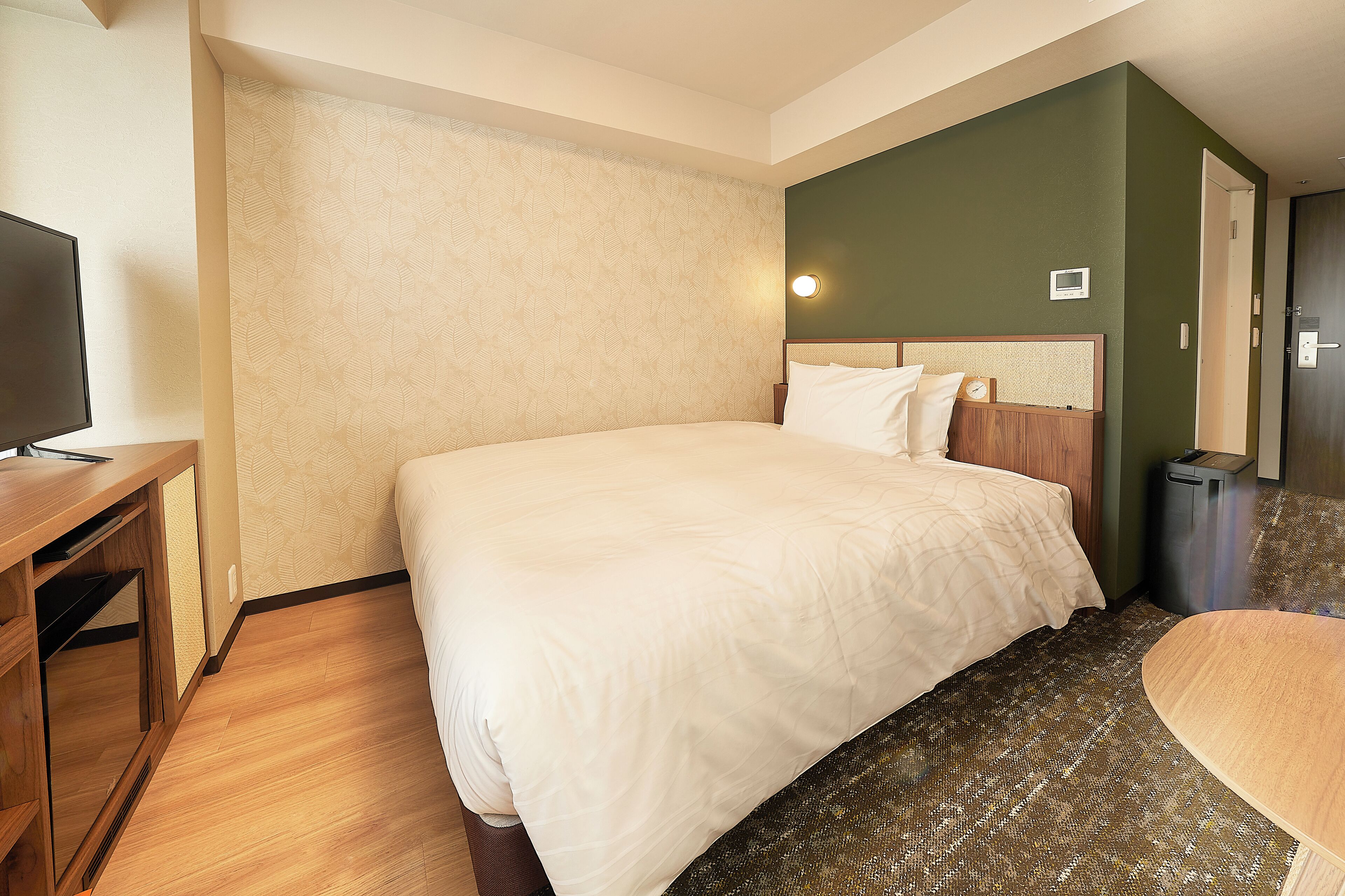 A hotel room with a bed, a desk, a television, and a door.