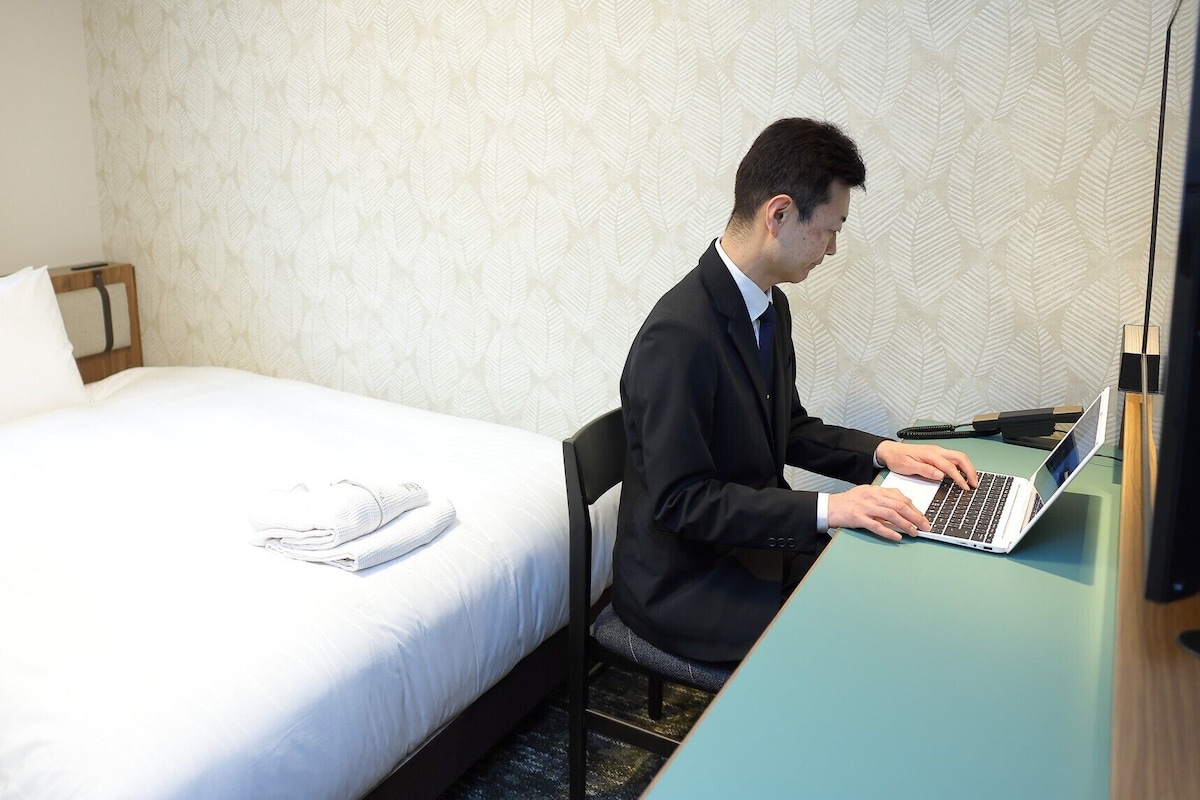 Una habitación de hotel con una cama, un escritorio con una computadora portátil y un teléfono.