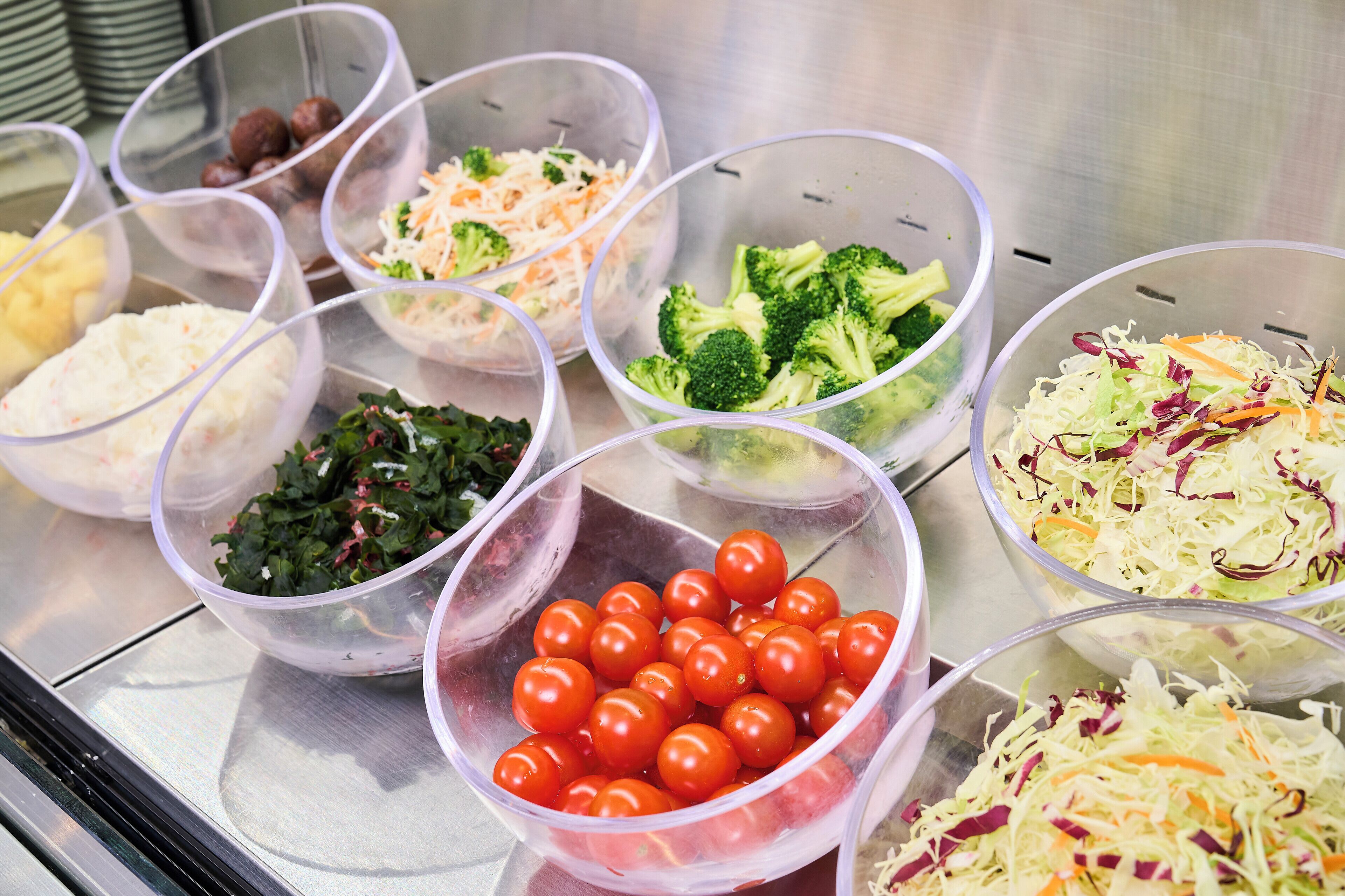 Diversos alimentos en recipientes transparentes, como tomates, brócoli y verduras ralladas.