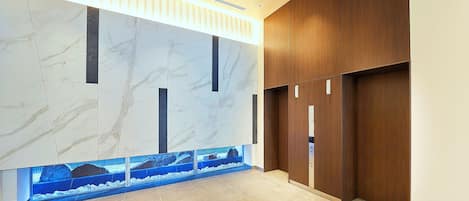 Un hall d’entrée moderne avec des murs en marbre, un mur recouvert de panneaux en bois et un aquarium intégré.