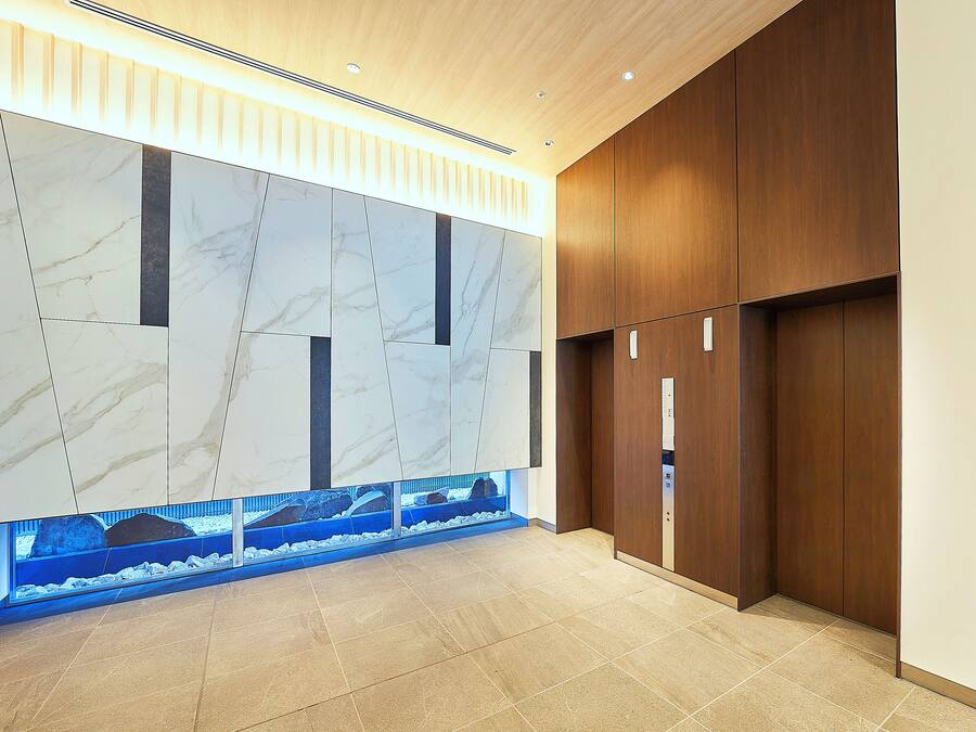 Um hall moderno com paredes de mármore, painel de madeira e um aquário embutido.