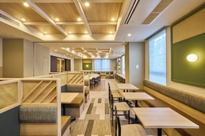 Un comedor moderno con mesas y bancos de madera, un techo alto con iluminación empotrada y ventanas grandes que dejan entrar luz natural.