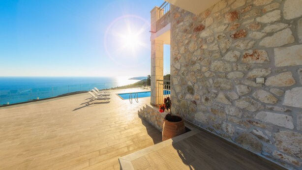 A stone wall with a view of the sea and a pool area with lounge chairs. - SeaFront Stone Villa with private access to the Beach (Άγιος Σώστης)