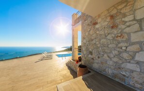 Un mur de pierre offrant une vue sur la mer et un espace piscine avec des chaises longues.