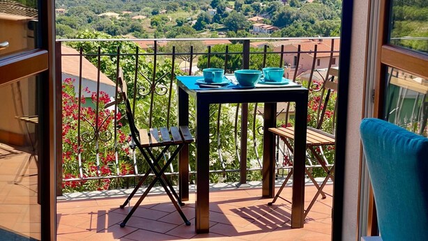 Un balcon avec une table et des chaises, donnant sur un paysage côtier avec des maisons et de la végétation.