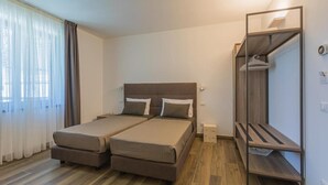 A double bed with a wooden headboard, a bedside table, and a mirror cabinet with a hanging coat rack. - Insula Felix Deluxe Double or Twin Room (Moniga del Garda)