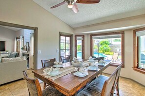 A dining area with a wooden table set for four, a ceiling fan, and large windows offering a view of the outdoors.