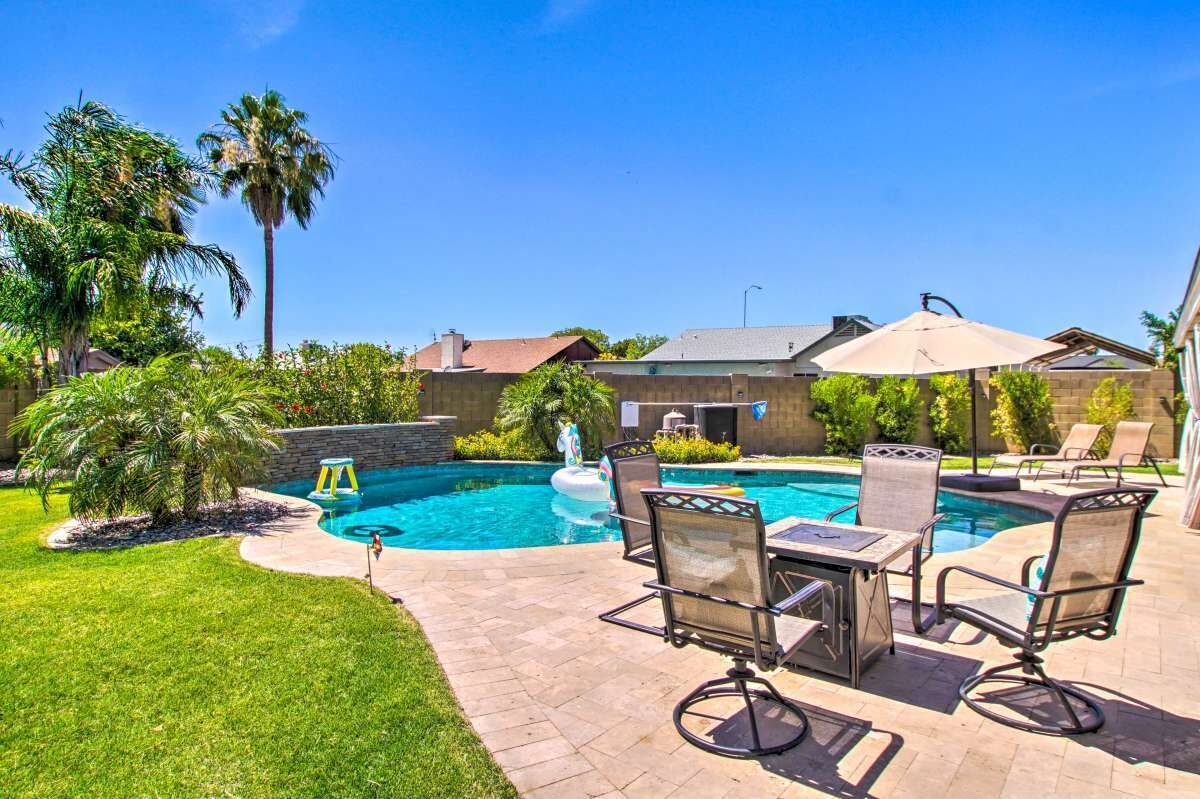 A backyard with a swimming pool, patio furniture, and a stone wall.