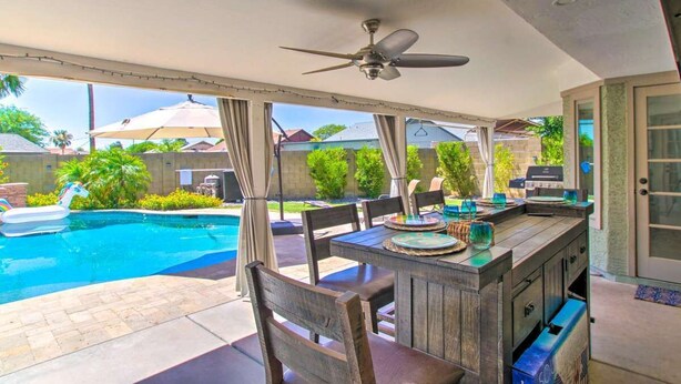Eine Terrassenanlage im Freien mit Pool, einer Holzbar und einem Deckenventilator.