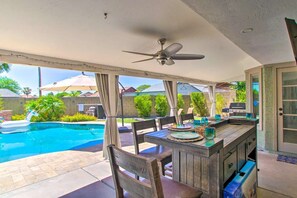 An outdoor patio with a pool, a wooden bar, and a ceiling fan.