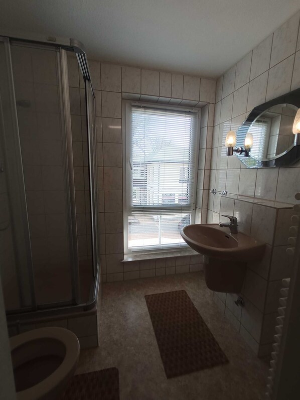 Un baño con ducha, inodoro, lavamanos y una ventana con persianas.