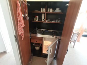 A compact kitchen with a sink, stove, and storage shelves.