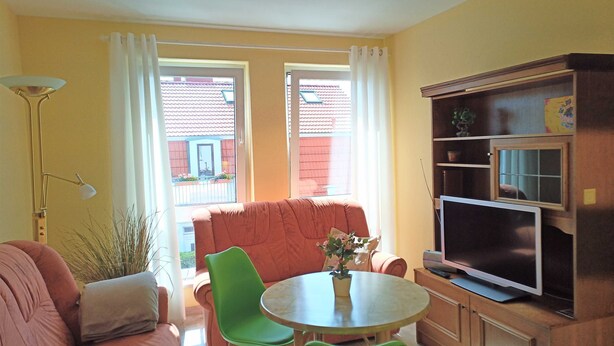 Een woonkamer met een bank, twee stoelen, een kleine tafel met een vaas, een televisie en een boekenkast.