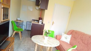 Een ruimtelijke leefruimte met een televisie, een eettafel met stoelen, een bank en een kitchenette.