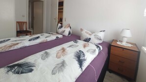 Een slaapkamer met twee bedden, een houten nachtkastje, een lamp en een kledingkast.