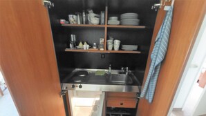 Een kleine keuken met een spoelbak, fornuis en opbergplanken.