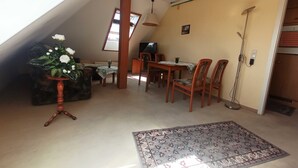 Een gezellig zolderkamer met een eettafel, stoelen, een televisie en een groot raam.