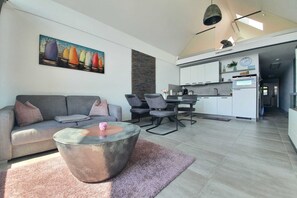 En moderne stue med sofa, sofabord og spiseområde. Et køkken er synligt i baggrunden.