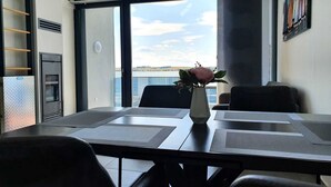 Un comedor con una mesa dispuesta para cuatro personas, un florero con flores y vistas al mar a través de amplios ventanales.
