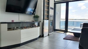 Una sala de estar moderna con un televisor de pantalla plana, un ventanal corredero que da a un balcón y un diseño minimalista.