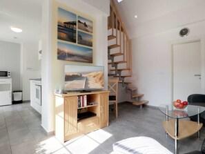 Uma sala de estar moderna com escada de madeira, TV de tela plana em um console de madeira e uma mesa de centro de vidro, com vista para o exterior.