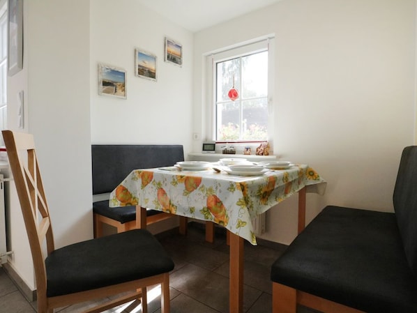 Uma área de refeições com uma mesa posta para quatro, uma janela com vista e uma cadeira com almofada.