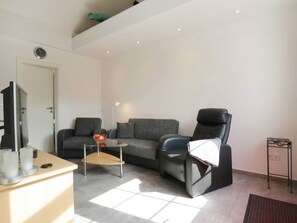 Uma sala de estar moderna com um sofá, uma poltrona, uma mesa de centro e uma televisão.