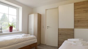 A bedroom with a bed, a wardrobe, a door, and a window with a plant. - Troja Ferienwohnung, Deutschland (Kalkhorst)