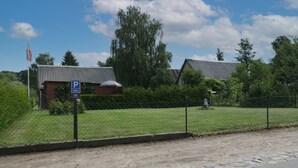 A building with a parking sign, a fenced area, and a grassy field. - Troja Ferienwohnung, Deutschland (Kalkhorst)
