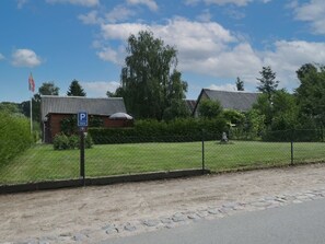 A building with a parking sign, a fenced area, and a grassy field. - Troja Ferienwohnung, Deutschland (Kalkhorst)