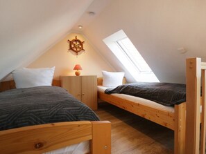 Ein kleines, gemütliches Schlafzimmer im Dachgeschoss mit zwei Holzbettstapeln, einem Holzschrank, einer Schiffsradausstellung und einem Oberlicht.