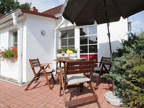 An outdoor patio with a table and chairs, a large umbrella, and a window with a view of a mountain.