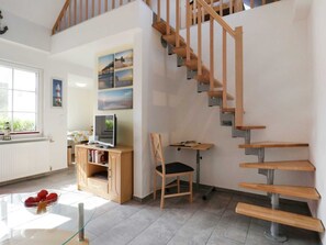 Un vaste espace de vie agrémenté d’un escalier en bois, d’un téléviseur posé sur un meuble en bois et d’une bibliothèque.