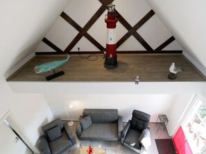 Quarto estilo loft com teto de madeira, um modelo de farol vermelho e branco, uma escultura de peixe azul-turquesa e uma pequena figura de pássaro.