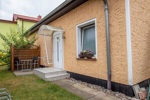 A house with a small patio, a door, a window with a flower box, and a visible gutter.