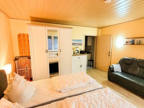A bedroom with a bed, a wardrobe, a kitchenette, and a leather sofa.