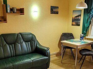 A living room with a green leather sofa, a dining table with chairs, a wall-mounted light, and a painting.