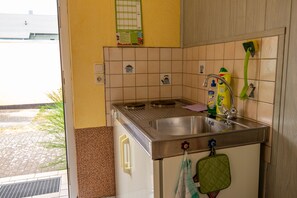 Une cuisine avec un évier en acier inoxydable, une brosse à manche vert et un pare-éclaboussures carrelé.