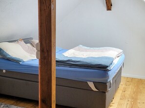 A bed with a grey mattress and blue bedding, a wooden headboard, and a plain wall. - Koje 6 - Ferientraum Zinnowitz (Zinnowitz)