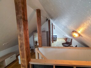 Dormitorio tipo loft con vigas de madera a la vista, una cama, un escritorio y una silla.