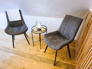 Twee grijze bekleden stoelen met zwarte metalen poten, een klein rond tafeltje met een glazen blad en een brandende kaars in het midden.